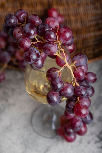 Copa de vino blanco con uvas rojas frescas sobre mesa de piedra.