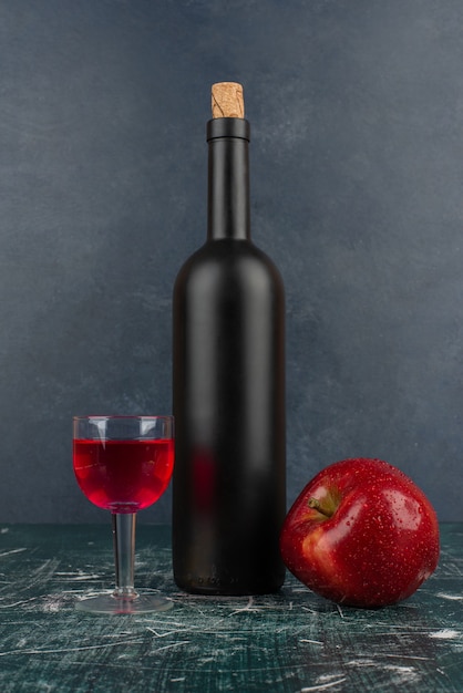 Copa de vino tinto y botella sobre mesa de mármol con manzana roja.