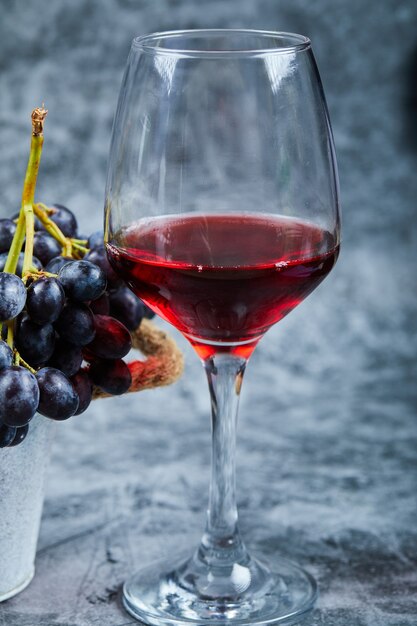 Una copa de vino tinto sobre un fondo de mármol con uvas. Foto de alta calidad