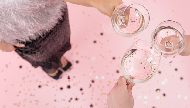 Copas con champagne en manos de las niñas en una fiesta sobre un fondo rosa, copie el espacio.