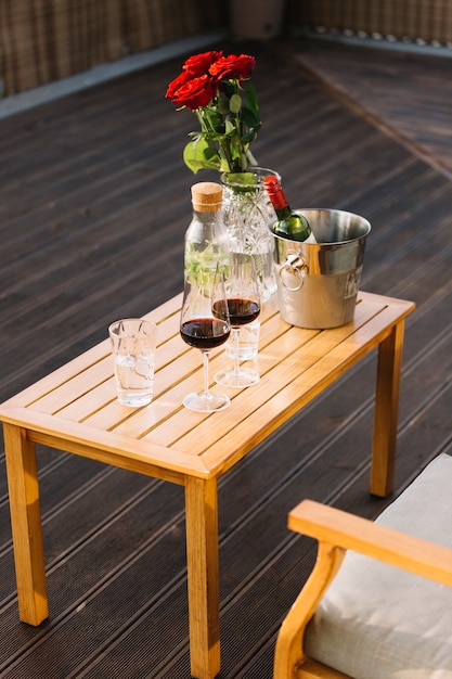 Copas de vino y cubo de hielo con botella de vino en la mesa de madera en el patio