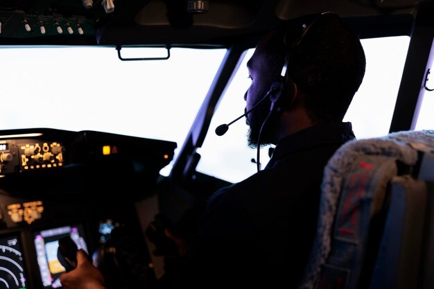 Copiloto afroamericano sosteniendo la palanca para despegar con avión, avión volador con botones de encendido del tablero y comando del panel de control. Radar de navegación y brújula de parabrisas. De cerca.