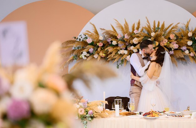 Cople en trajes de boda besándose cerca de la mesa festiva