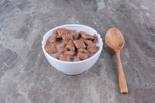 Copos de chocolate copos de maíz en un tazón blanco con una cuchara de madera.