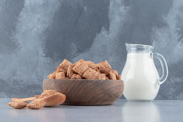 Copos de maíz de almohadillas de chocolate en un tazón de madera con una botella de leche. Foto de alta calidad