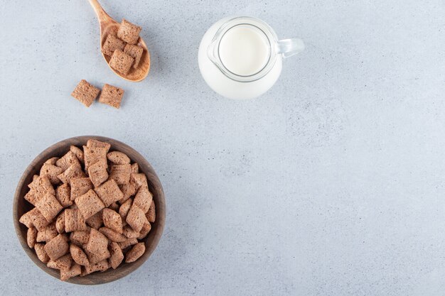 Copos de maíz de almohadillas de chocolate en un tazón de madera con una botella de leche. Foto de alta calidad