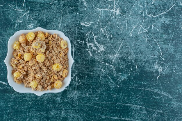 Copos de maíz deliciosos en un cuenco, sobre la mesa azul.