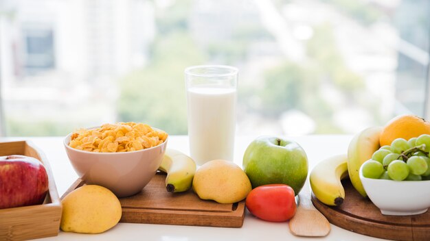 Copos de maíz; frutas vaso de leche en la mesa cerca de la ventana