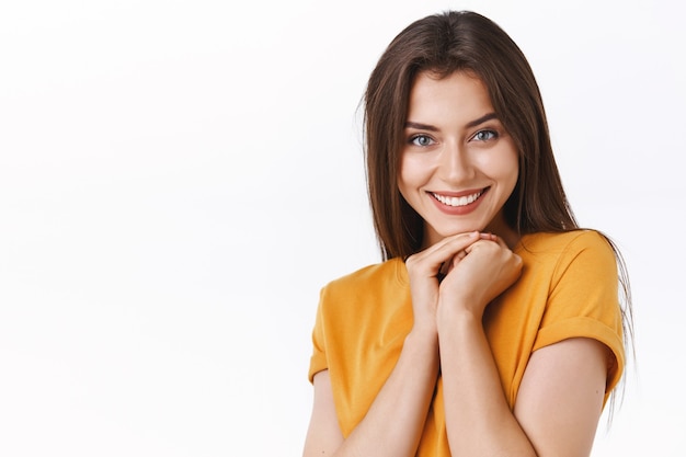 Coqueta atractiva novia feliz recibe un regalo encantador y caro, sonriendo con alegría, recibe lo deseado, estrecha las manos cerca de la línea de la mandíbula en una pose femenina coqueta, de pie fondo blanco