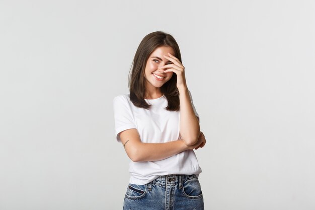 Coqueta hermosa chica cubre la cara con la mano mientras se ríe y mira la esquina superior izquierda.