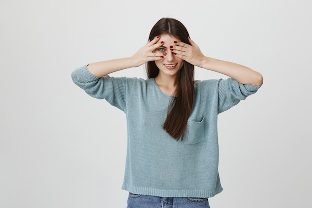 Foto gratuita coqueta mujer sonriente cubre los ojos y mira entre los dedos