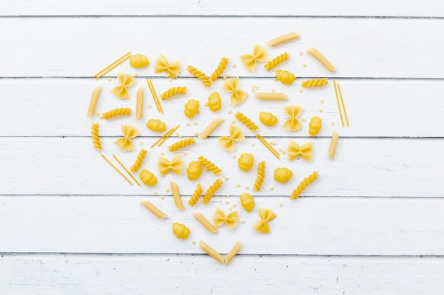 Foto gratuita corazón hecho por diferentes tipos de pasta en mesa de madera