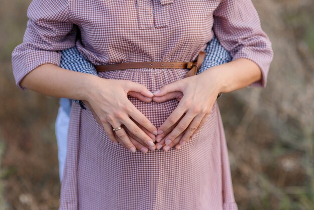 Corazón hecho de manos en el vientre de la mujer embarazada casada