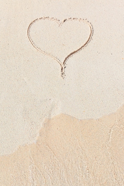 Corazón manuscrito en arena con ola acercándose en la playa
