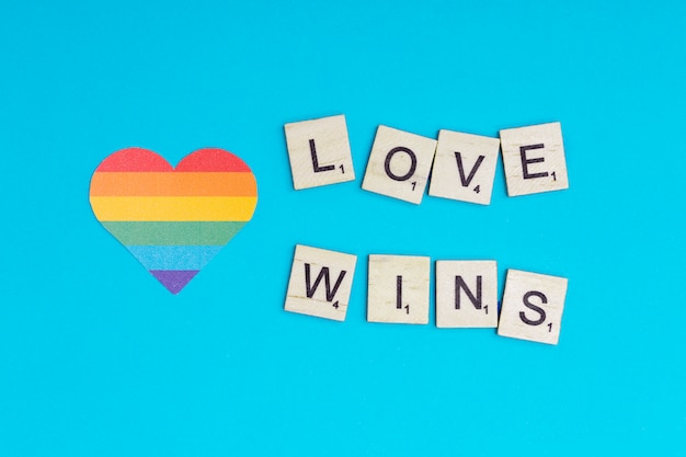 Corazón multicolor LGBT con lema LOVE WINS sobre fondo azul