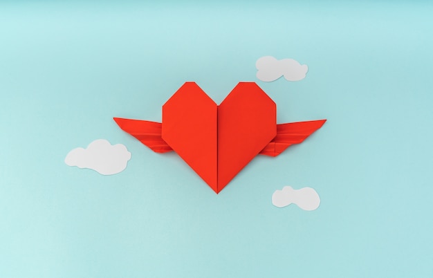 Foto gratuita corazón del origami de papel rojo con las alas y la nube sobre fondo azul