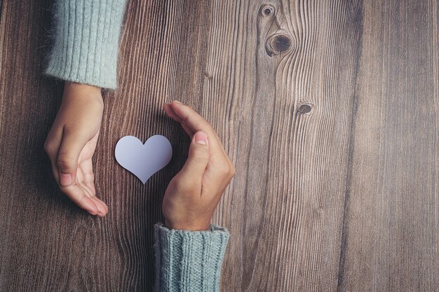 Corazón de papel y las manos de la pareja en la mesa de madera