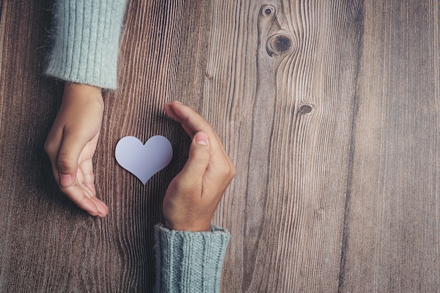 Corazón de papel y las manos de la pareja en la mesa de madera