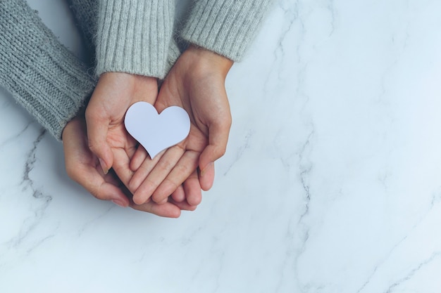 Corazón de papel puesto en manos de la pareja sobre la mesa de mármol