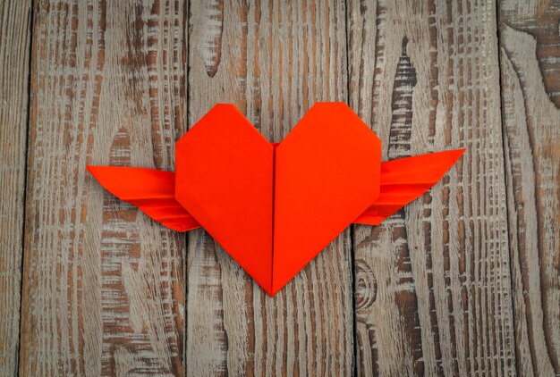 corazón rojo del origami de papel con las alas en el fondo de madera.