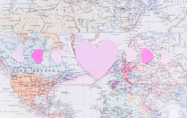 Corazones de papel brillantes pequeños en el mapa del mundo