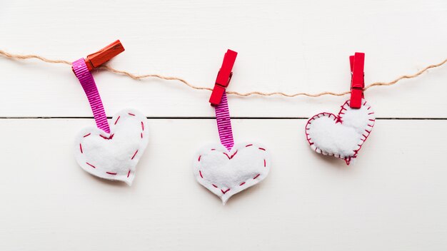 Corazones de puntada blanca en una cuerda atada con pinzas rojas en una cuerda contra un tablón de madera