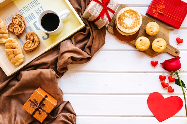 Corazones y rosa cerca de regalos y desayuno