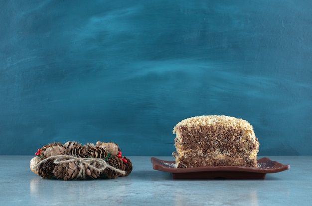Corona de cono de pino junto a un plato con una rebanada de pastel sobre la superficie de mármol