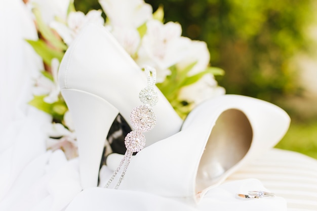 Corona de diamantes sobre el par de tacones de boda blancos con anillos en la mesa