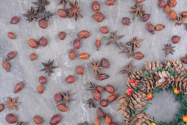 Corona festiva de Navidad con piñas y anís estrellado sobre fondo de mármol.