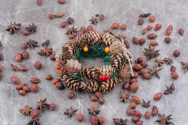 Corona festiva de Navidad con piñas y anís estrellado sobre fondo de mármol.