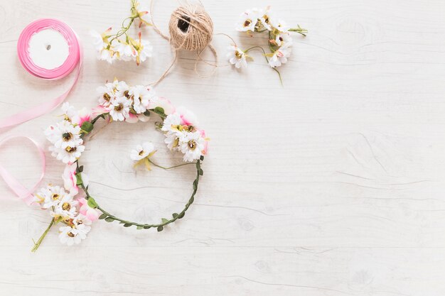 Corona de flores; carrete de cuerda y cinta rosada sobre fondo texturizado