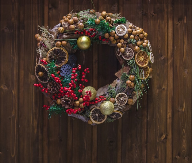 Corona de Navidad con bayas de acebo y rodaja de naranja seca colgada en la puerta