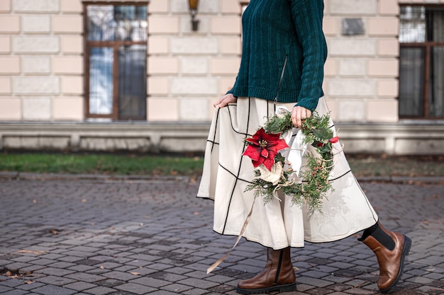 Corona de Navidad en manos de una mujer elegante a pie de la ciudad