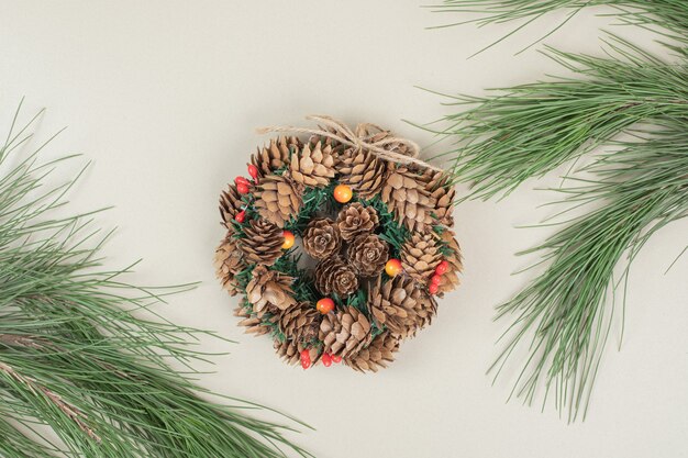 Corona navideña decorada con piñas y bayas de acebo