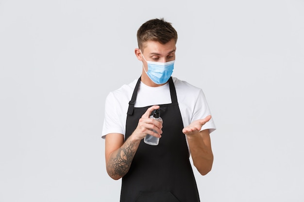 Coronavirus, distanciamiento social en cafés y restaurantes, concepto empresarial durante la pandemia. barista, empleado de la tienda desinfectando las manos con desinfectante de manos, camarero trabajando en máscara médica