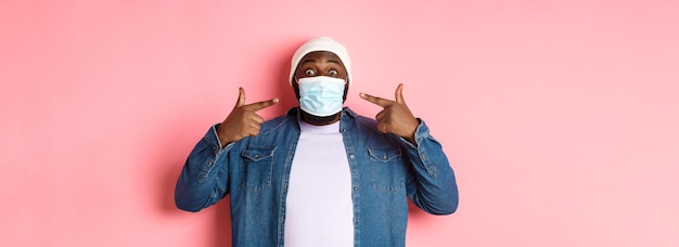 Foto gratuita coronavirus estilo de vida y concepto de distanciamiento social hombre negro feliz en beanie apuntando a su cara m