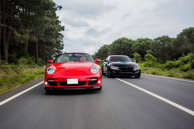 Corre en la carretera entre autos coupé negros y rojos.