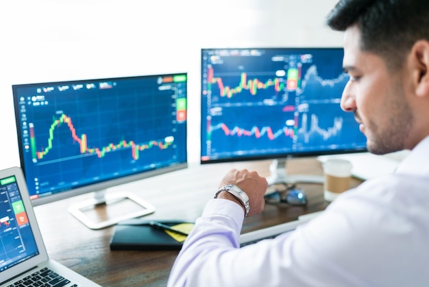 Corredor de bolsa masculino confiado esperando que se abra el mercado de valores y mirando su reloj frente a su computadora