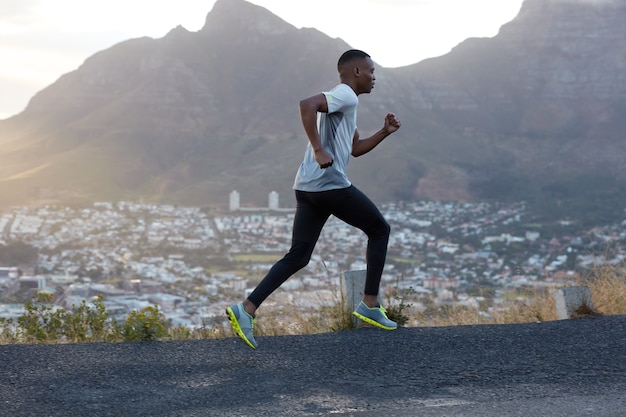 El corredor masculino atlético en forma corre rápido por la carretera, hace ejercicio al aire libre, un paisaje de montaña increíble, respira aire fresco, vestido con ropa informal para el deporte. Concepto de personas y recreación