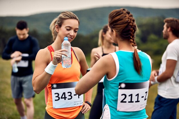 Corredoras comunicándose antes de la carrera de maratón en la naturaleza El foco está en la mujer con una botella de agua