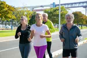 Foto gratuita corredores maduros felices y cansados en ropa deportiva corriendo afuera, entrenando para maratón, disfrutando del entrenamiento matutino. personas jubiladas y concepto de estilo de vida activo.