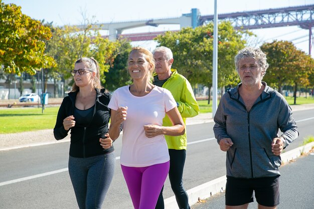 Corredores maduros felices y cansados en ropa deportiva corriendo afuera, entrenando para maratón, disfrutando del entrenamiento matutino. Personas jubiladas y concepto de estilo de vida activo.