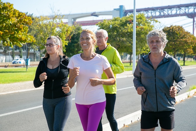 Corredores maduros felices y cansados en ropa deportiva corriendo afuera, entrenando para maratón, disfrutando del entrenamiento matutino. Personas jubiladas y concepto de estilo de vida activo.