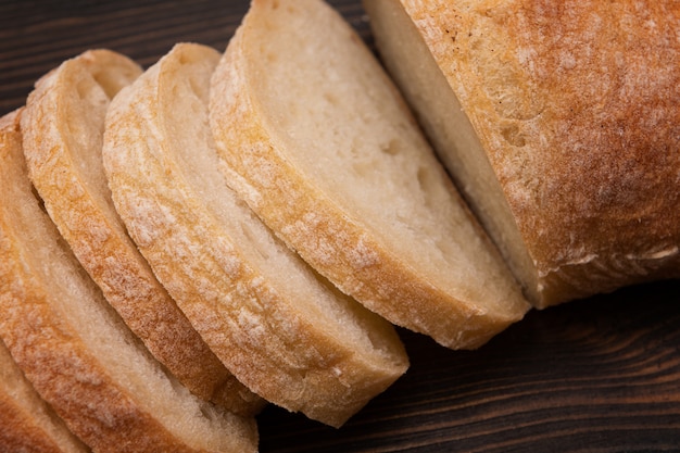 Cortando el ciabatta cerca para arriba en fondo de madera.