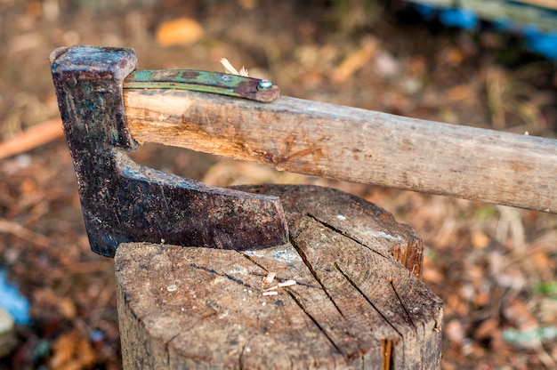 Cortando madera con hacha. Hacha atascada en un tronco de madera. Macho viejo, desgastado, rayado, sostenido de pie en un tronco de árbol de madera, agrietado sobre un fondo de madera picada.