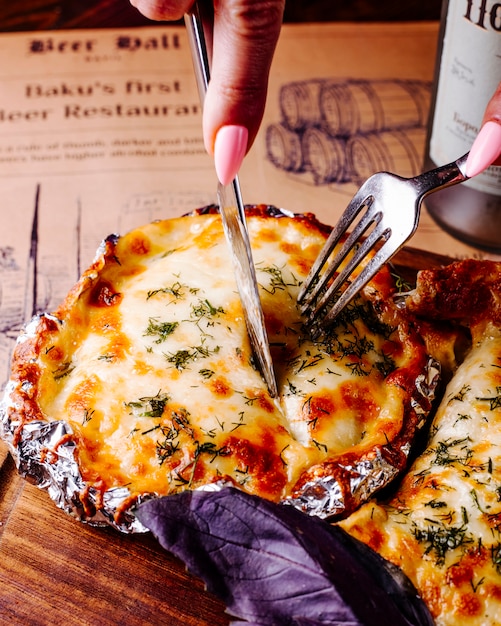 Cortar alimentos con queso derretido y hierbas con cubiertos.