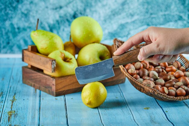 Cortar limón en mesa azul con canasta de madera de manzanas y nueces.