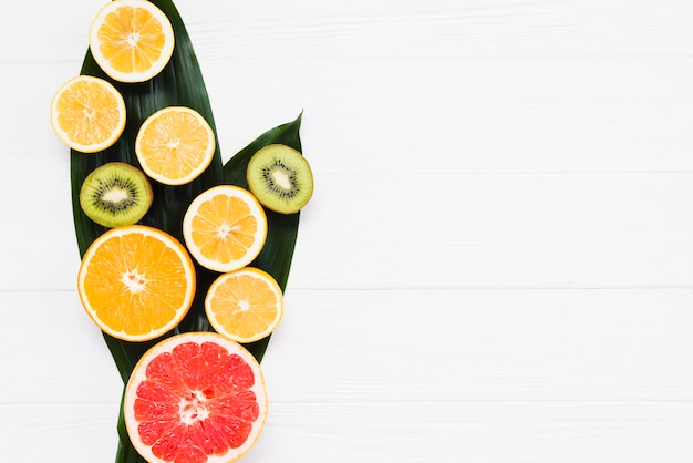 Corte de frutas exóticas frescas en hojas de plátano sobre fondo blanco