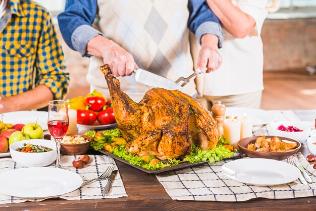 Corte humano de pollo asado en bandeja cerca de personas